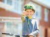 Un bambino con casco e bicicletta sorride verso l’obiettivo con il pollice alto