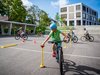 Un élève effectue un parcours à vélo sur la place de l’école. Il se concentre pour positionner correctement la balle.